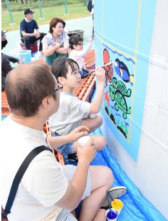 風車タワーをキャンバスに、色鮮やかに海の世界を描く参加者（能代港大森緑地広場で）