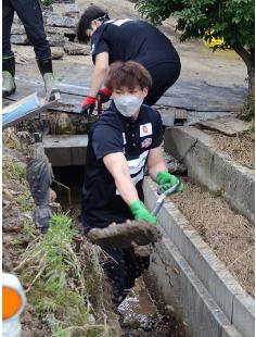 側溝にたまった泥のかき出し作業を行うハピネッツの長谷川選手（能代市二ツ井町梅内で）