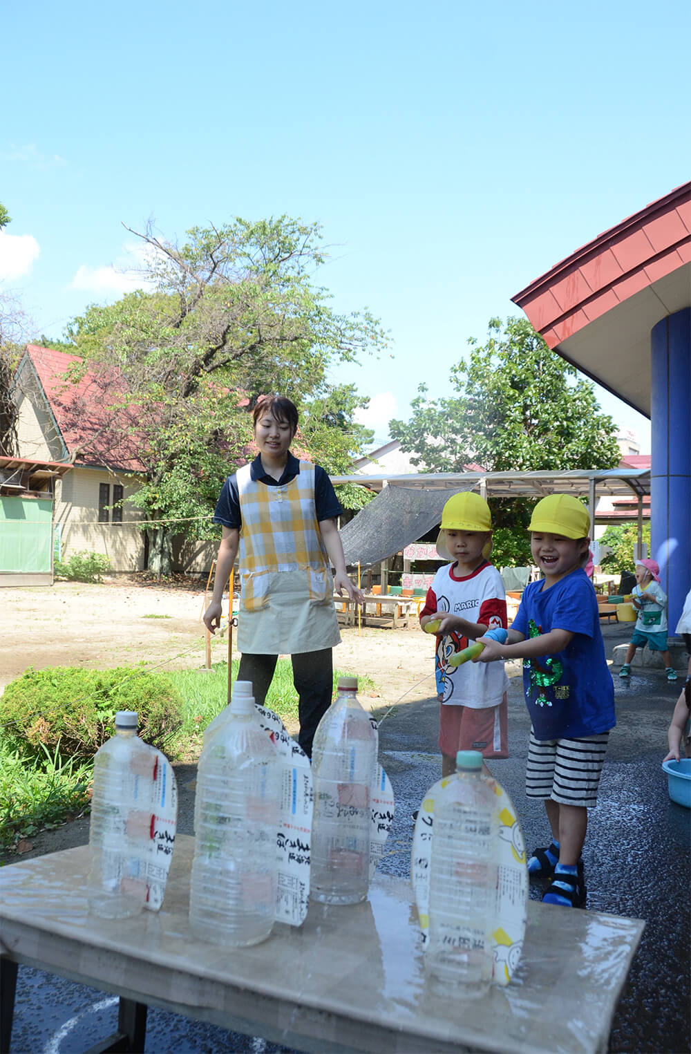 園庭の日陰スペースで水遊びを楽しむ子どもたち（能代市柳町の渟城幼稚園で）